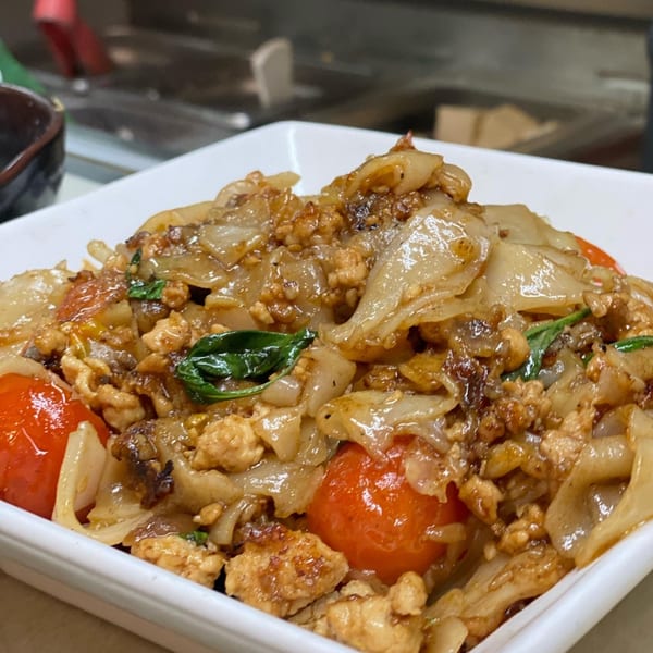 Close-up of Thai Basil's Pad See Ew with wide noodles, chicken, tomatoes, and basil.