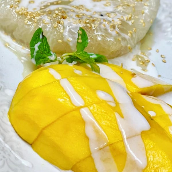 Thai Basil's mango sticky rice dessert, topped with coconut milk, sesame seeds, and a mint sprig.