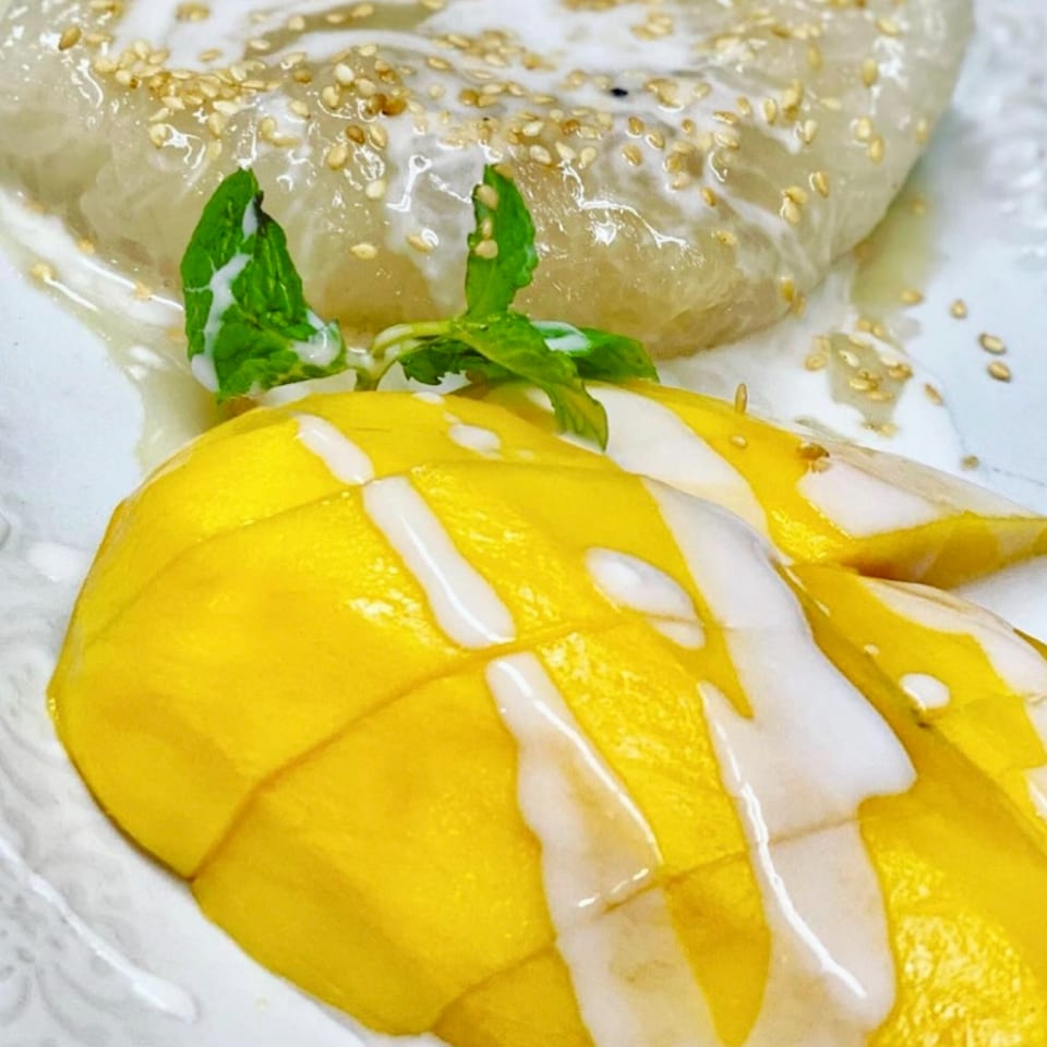 Thai Basil's mango sticky rice dessert, topped with coconut milk, sesame seeds, and a mint sprig.