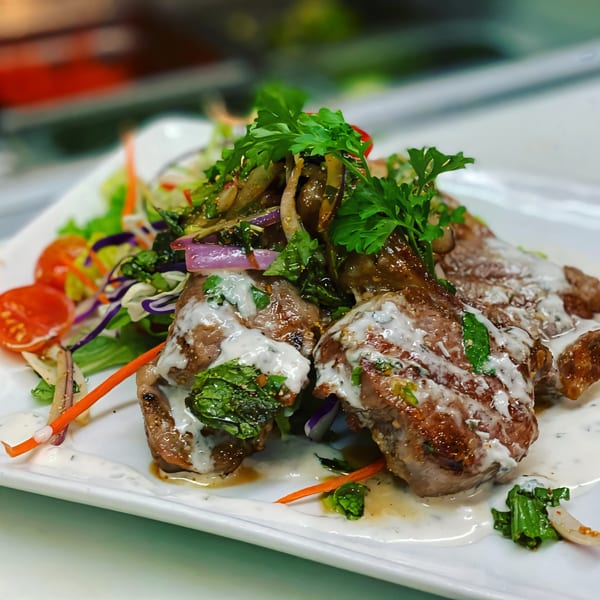 Grilled Thai Basil lamb chops with creamy sauce, fresh herbs, and a side salad.