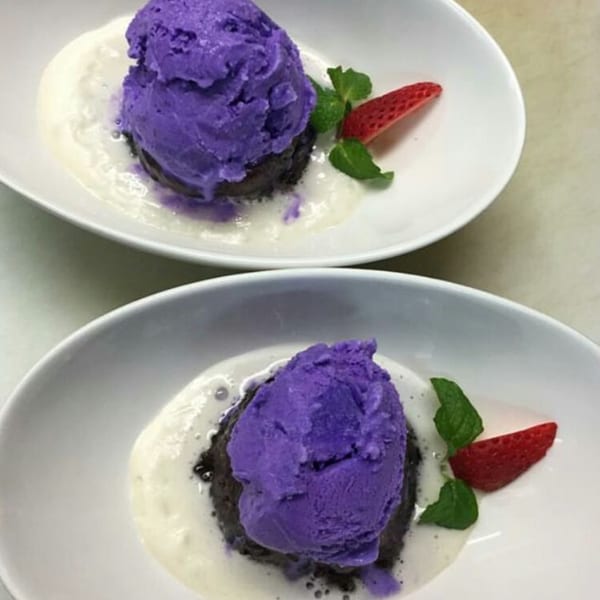 Two plates of purple ube ice cream on dark cake with cream, garnished with mint and strawberry.