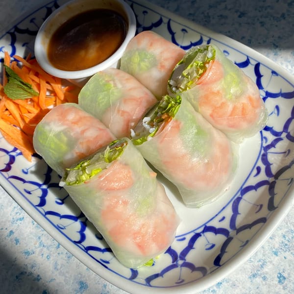 Six Thai Basil fresh spring rolls with shrimp, lettuce, and rice noodles, served with peanut sauce and shredded carrots.