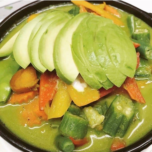 Thai Basil's green curry with sliced avocado, bell peppers, carrots, and okra in a black bowl.