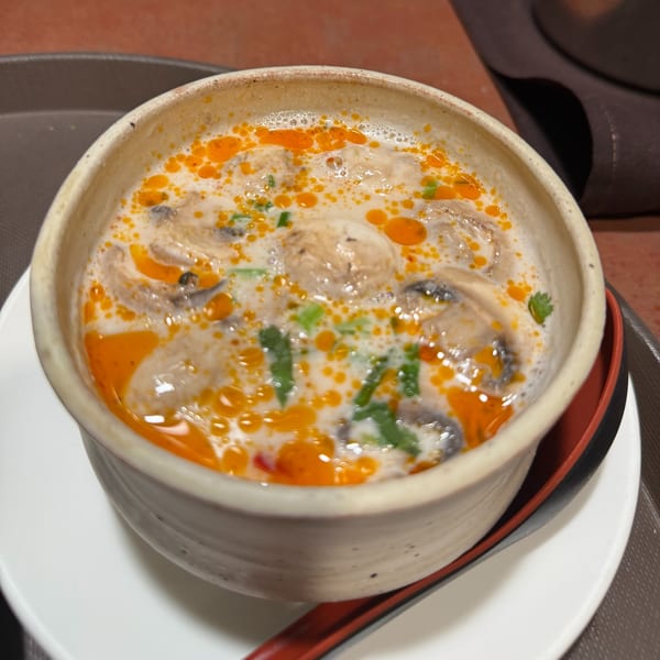 Creamy Tom Kha Gai soup with mushrooms, chili oil, and cilantro in a ceramic bowl.
