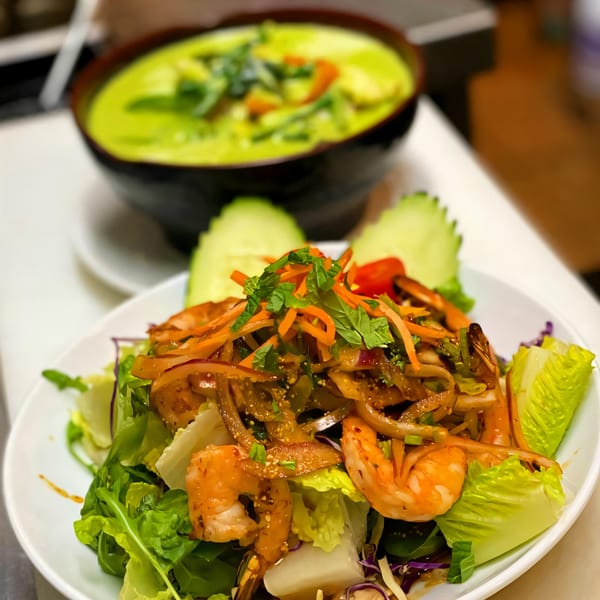 Thai Basil's shrimp salad with fresh greens, carrots, and herbs, with green curry in the background.